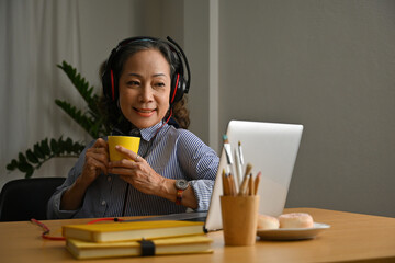 Old senior woman in headphones listening music or podcast feel peace of mind at home.