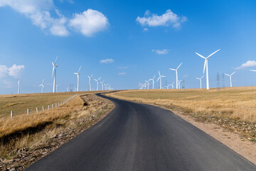 Empty asphalt highway road surrounded by fields with windmills