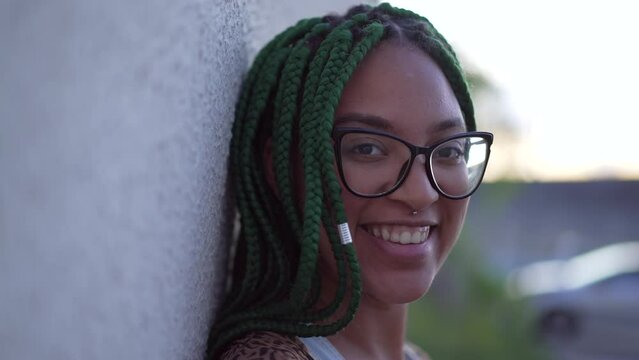 Portrait of a Brazilian young woman with braided hairstyle closeup face looking at camera smiling. A black latina adult girl with green box braids hair