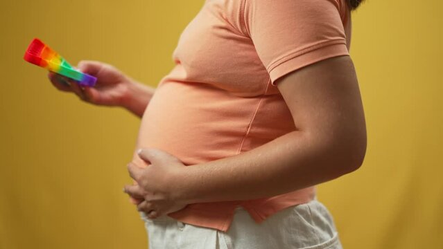 Side view unrecognizable pregnant woman playing fidget toy in slow motion caressing belly. Young Caucasian expectant stroking tummy popping dimples in and out at yellow background