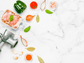 Manual retro meat grinder with raw meat and vegetables on a marble table.