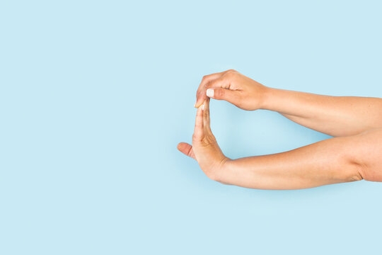 Manos de mujer haciendo un gesto de estiramiento con los dedos sobre un fondo celeste pastel liso y aislado. Vista de frente y de cerca. Copy space