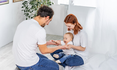Obraz premium dad and mom play with their son. a child in a white t-shirt and blue jeans crawls on the floor. family in studio or at home