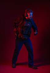soldier in full gear with weapons. a man in headphones, body armor, with a backpack and a belt. red background. colored, blue-red light