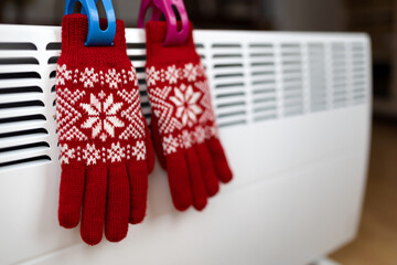 Christmas gloves on a warm heater radiator in a cold winter day at home. Power saving, energy crisis background.