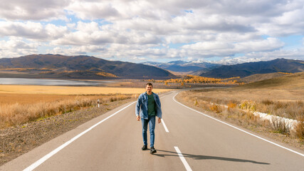 a man walks along an autumn road. the guy in jeans in autumn