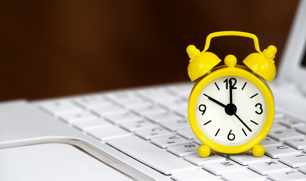 Yellow Alarm Clock On A White Laptop. Daylight Savings Time Banner Or Background.