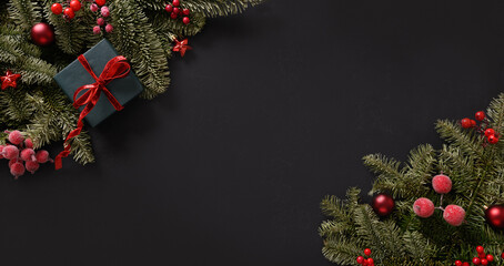 Christmas winter banner with fir branches, red balls on black background. Xmas greeting card. Holiday time. Happy New Year. Space for text. View from above, flat lay.