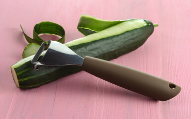 Knife for cleaning vegetables and fruits with cucumber with peeled skin on a pink background. Selective focus.