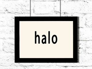 Black frame hanging on white brick wall with inscription halo