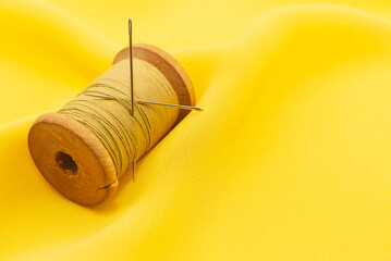 Old retro sewing accessories lie on a yellow fabric. Needle and thread