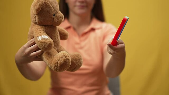 Close-up teddy bear and fidget toy in female Caucasian hands showing off. Unrecognizable blurred young woman showing sensory toy in slow motion at yellow background