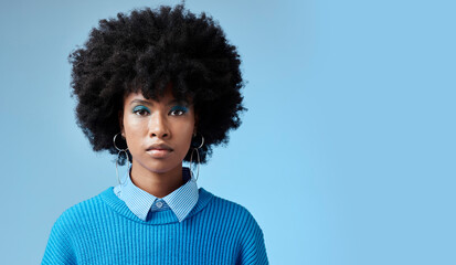 Portrait of black woman, fashion afro and serious face with an expression of focus on blue background studio mockup. Trendy earing accessory, stylish cool clothing and blue cosmetic eyeshadow makeup
