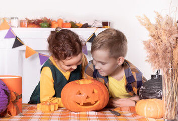 Fototapeta premium Young kids girl and boy carving traditional Halloween jack-o-lanterns with scary face for party at home