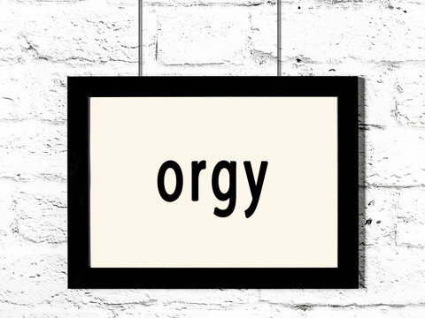 Black frame hanging on white brick wall with inscription orgy