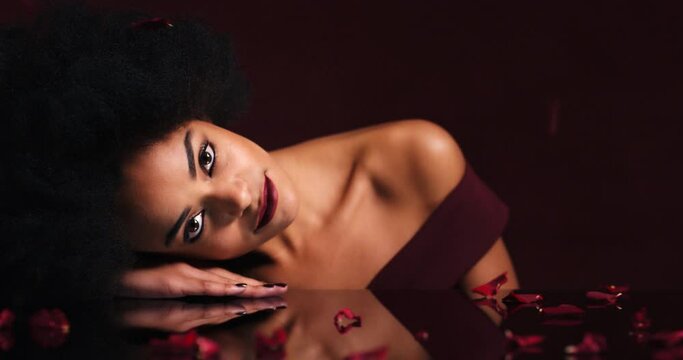 Face, petals and red roses for fashion model on studio table of Ethiopian woman with lipstick makeup cosmetics. Beauty portrait, people or flowers in creative luxury art of romance, skincare or love