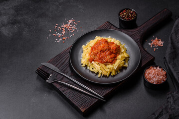 Obraz na płótnie Canvas Pasta with beef meatballs in tomato sauce with spices and herbs on a dark background