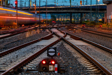 Twilight atmosphere at Hagen Main station Germany with many lights, signals and trains in motion. Catenary, glistening tracks, switches at blue hour. Railway infrastructure and technology at night.