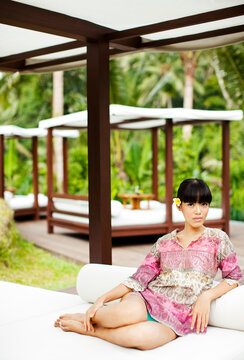 Young Asian Woman Lounging In A Hotel Pool Cabana, Ubud, Bali, Indonesia.