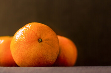 three ripe orange tangerines on a brown background with a shallow depth of field. selective focus on the mandarin stalk.
