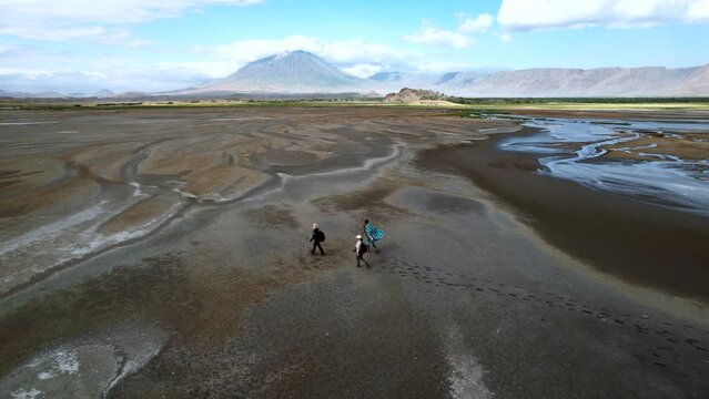 Aerial static view of tourist couple with Maasai guide exploring Lake Natron and Ol Doinyo Lengai Volcano, Tanzania