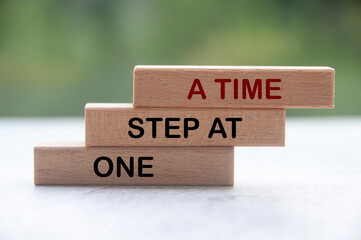 One step at a time words on wooden blocks with blurred nature background. Work completion concept.