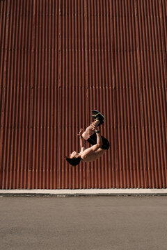 Vertical side view long shot of shirtless young man exercising outdoors levitating in backflip, copy space