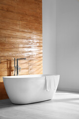 Fototapeta na wymiar White bathtub with towel near wooden wall in room