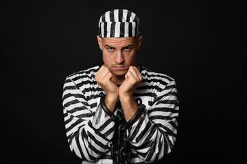 Prisoner in striped uniform with chained hands on black background