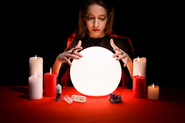 Soothsayer using glowing crystal ball to predict future at table in darkness. Fortune telling
