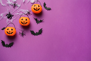 Flat lay composition with plastic pumpkin baskets, paper bats and spiders on purple background,...