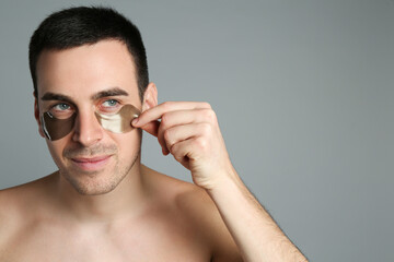 Fototapeta na wymiar Young man applying under eye patches on grey background. Space for text