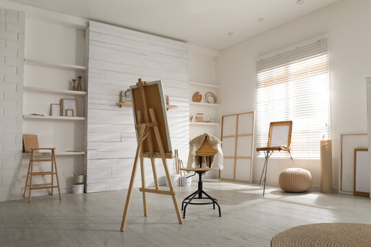 Modern studio interior with artist's workplace and foldable wooden easel near large window