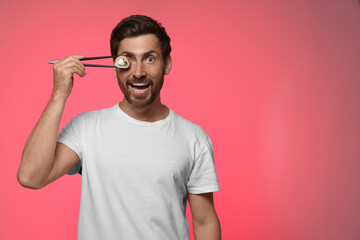 Funny man hiding his eye with tasty sushi roll on pink background. Space for text