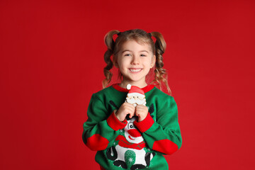 Cute little girl with Christmas gingerbread cookie on red background