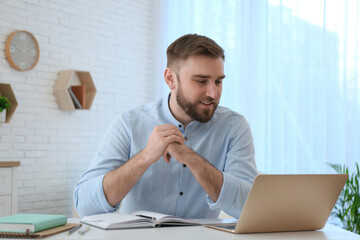 Young man watching online webinar at table indoors