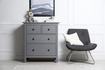 Stylish room interior with grey chest of drawers and comfortable chair