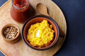 Sweet pumpkin porridge in clay bowl with jam and nuts