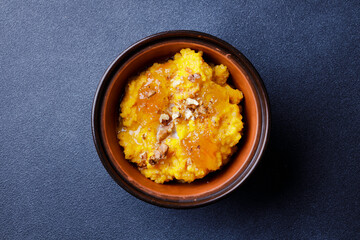 Sweet pumpkin porridge in clay bowl with jam and nuts