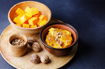 Sweet pumpkin porridge in clay bowl with jam and nuts and raw pumpkin cubes