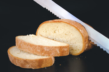 Knife slicing freshly baked loaf of bread. Dark food photo. Selective focus. Toned.
