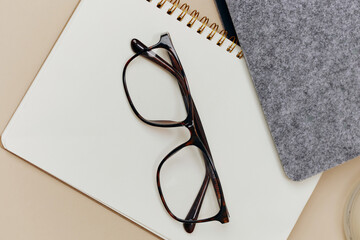 Closeup cropped shot of brown stylish classic unisex eyewear leans on notebooks on over pastel beige background. Fashion glasses ad. Copy space