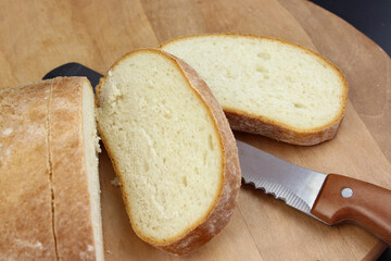 Knife is cutting a loaf of bread into slices. Cut fresh bread with a knife.