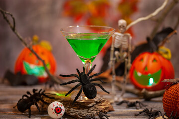 Halloween drinks green cocktail martini for party hand in glove holds glass on festive background.