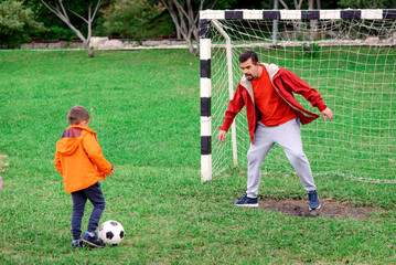 Father and toddler playing football at soccer field. Focus on father. Dad is standing at gates, kid...