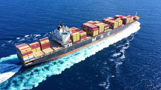 Aerial drone video of MSC truck size container cargo vessel cruising in deep blue sea near commercial port of Piraeus, Attica, Greece