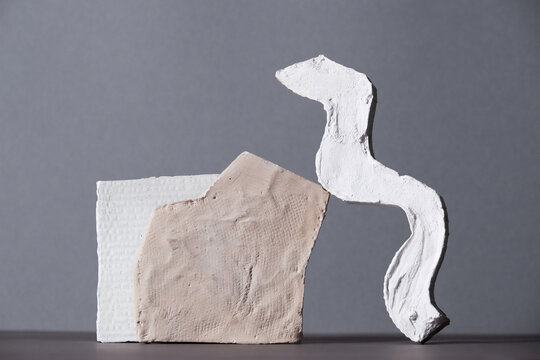 Horizontal close-up studio shot of contemporary still life installation of two white gypsum objects on gray background