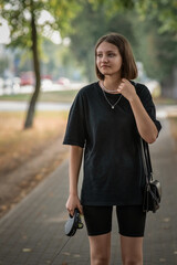 Obraz premium Portrait of a young beautiful fair-haired girl in dark clothes on the street of a summer city.