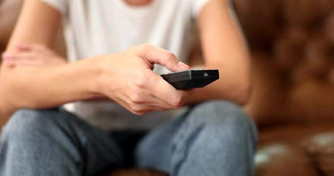 Woman sitting on couch changes channel with remote control