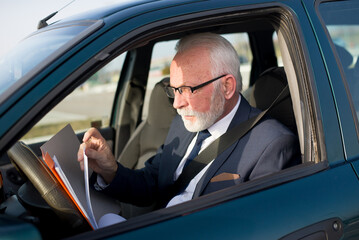 Senior businessman reading documents in the car on a sunny day